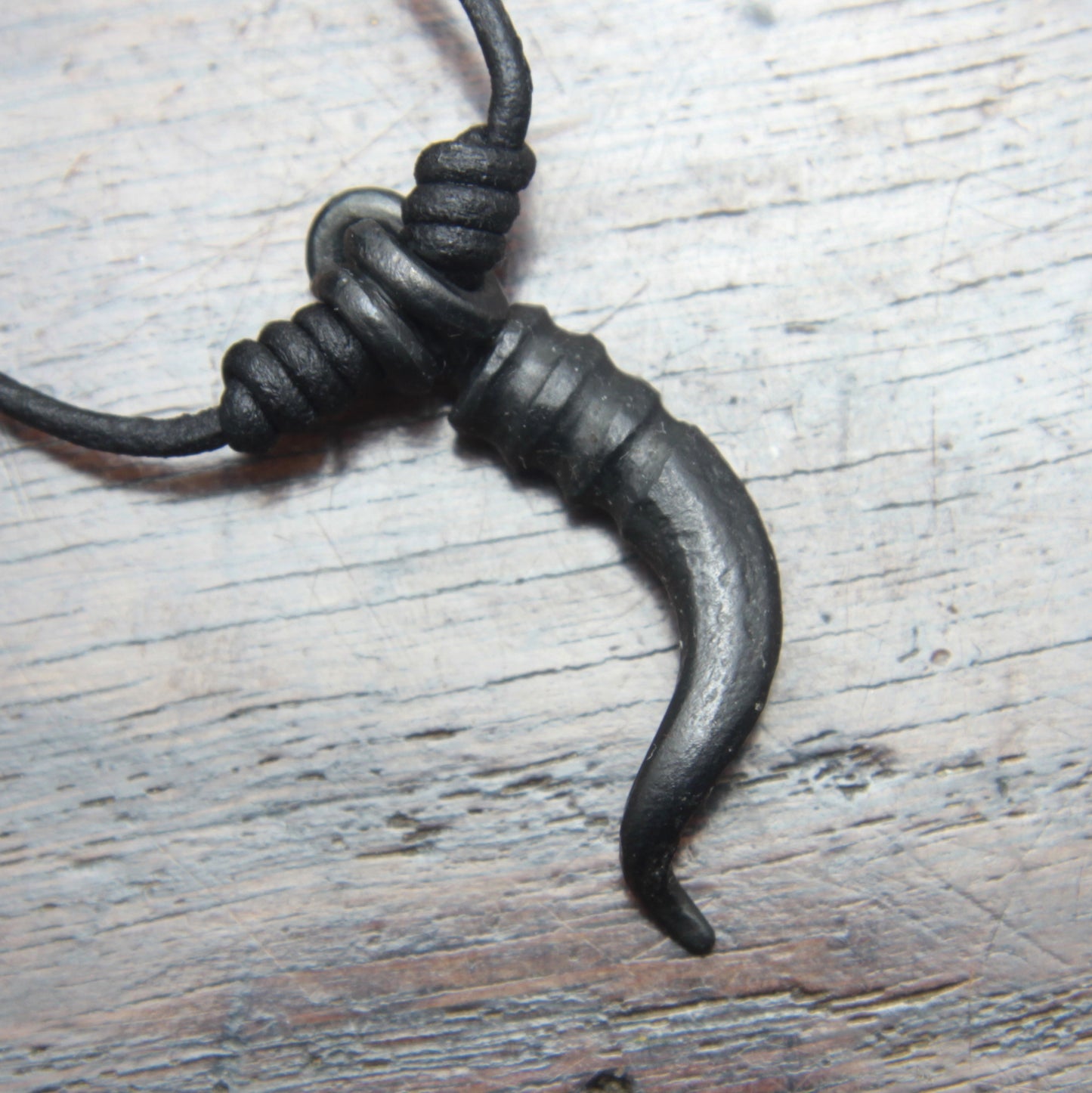 A forged iron cornicello, Italian horn, pendant with a black finish, on a black leather cord, designed and made by M Barran at Taitaya Forge. Back of the pendant