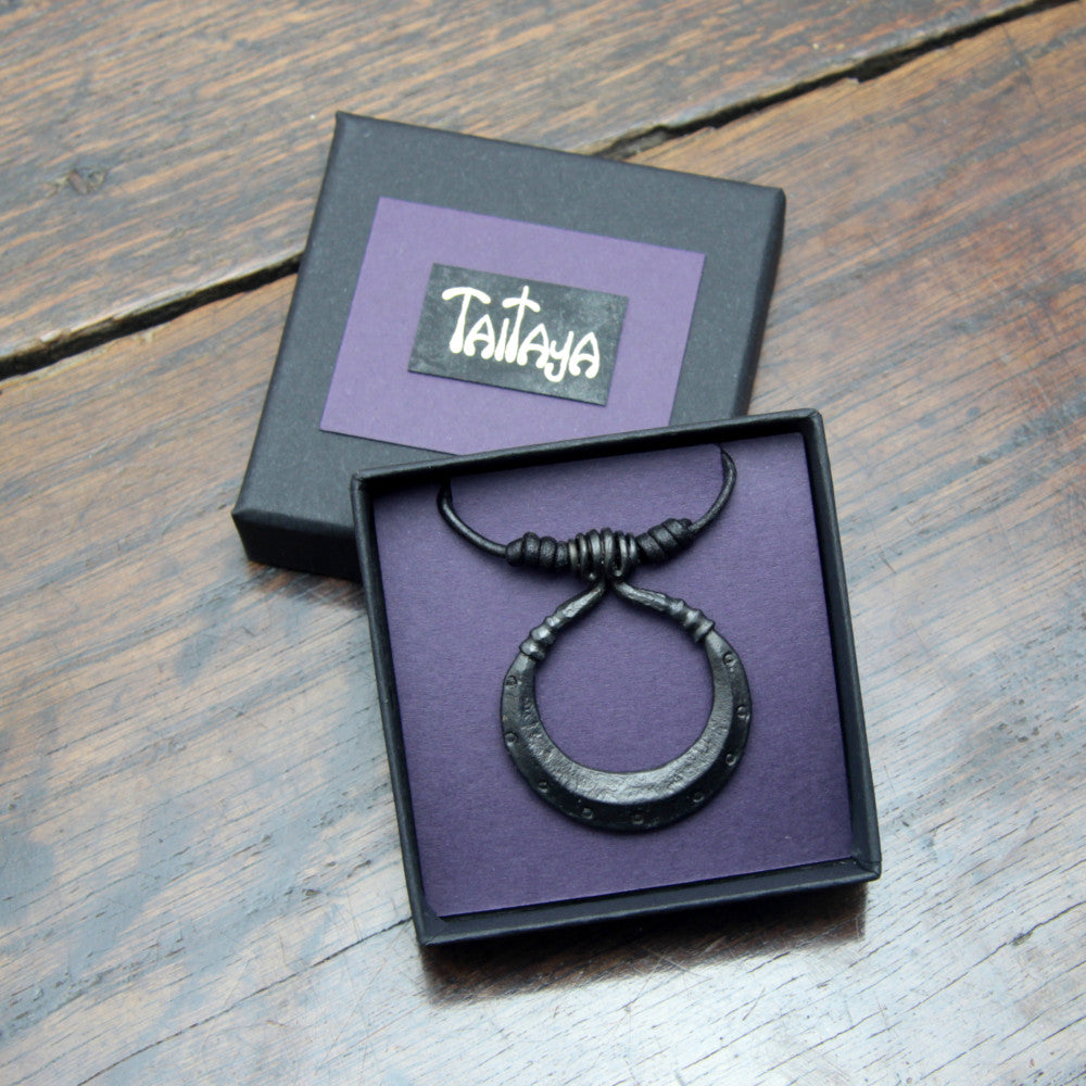 Handforged iron moon crescent pendant made by taitaya forge, presented in a small square black card gift box with gold embossed branding and purple insert.