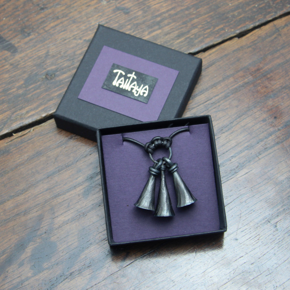 Handforged iron shaman bell pendant made by taitaya forge, presented in a small square black card gift box with gold embossed branding and purple insert.