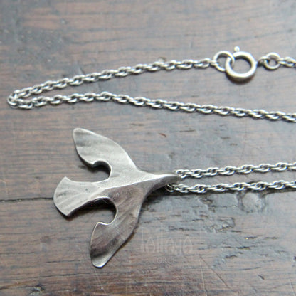 A silver raven pendant necklace featuring a stylized bird on a delicate chain, displayed on a dark wooden surface. Showing Spring ring clasp. 