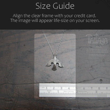 Silver raven pendant necklace displayed on a clear measurement card over a dark wood background, with a ruler at the bottom and a black header reading 'Size Guide' and instructions about aligning the frame with a credit card.