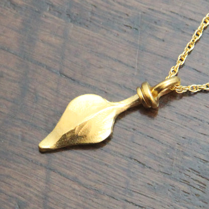 Gold colour leaf-shaped silver pendant on a rope chain against a wooden background