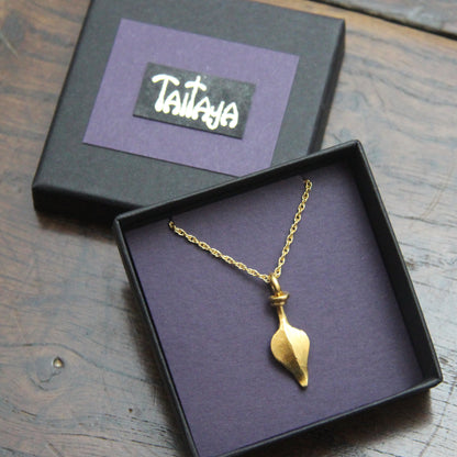 Gold necklace with a leaf pendant in a black and purple card jewelry box on a wooden surface, with 'Taitaya' branding.