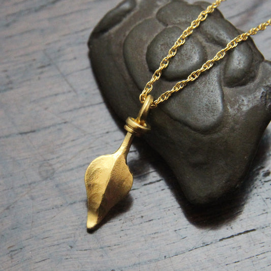 Gold colour leaf pendant necklace with a rope chain on a dark wooden suface resting on a stone