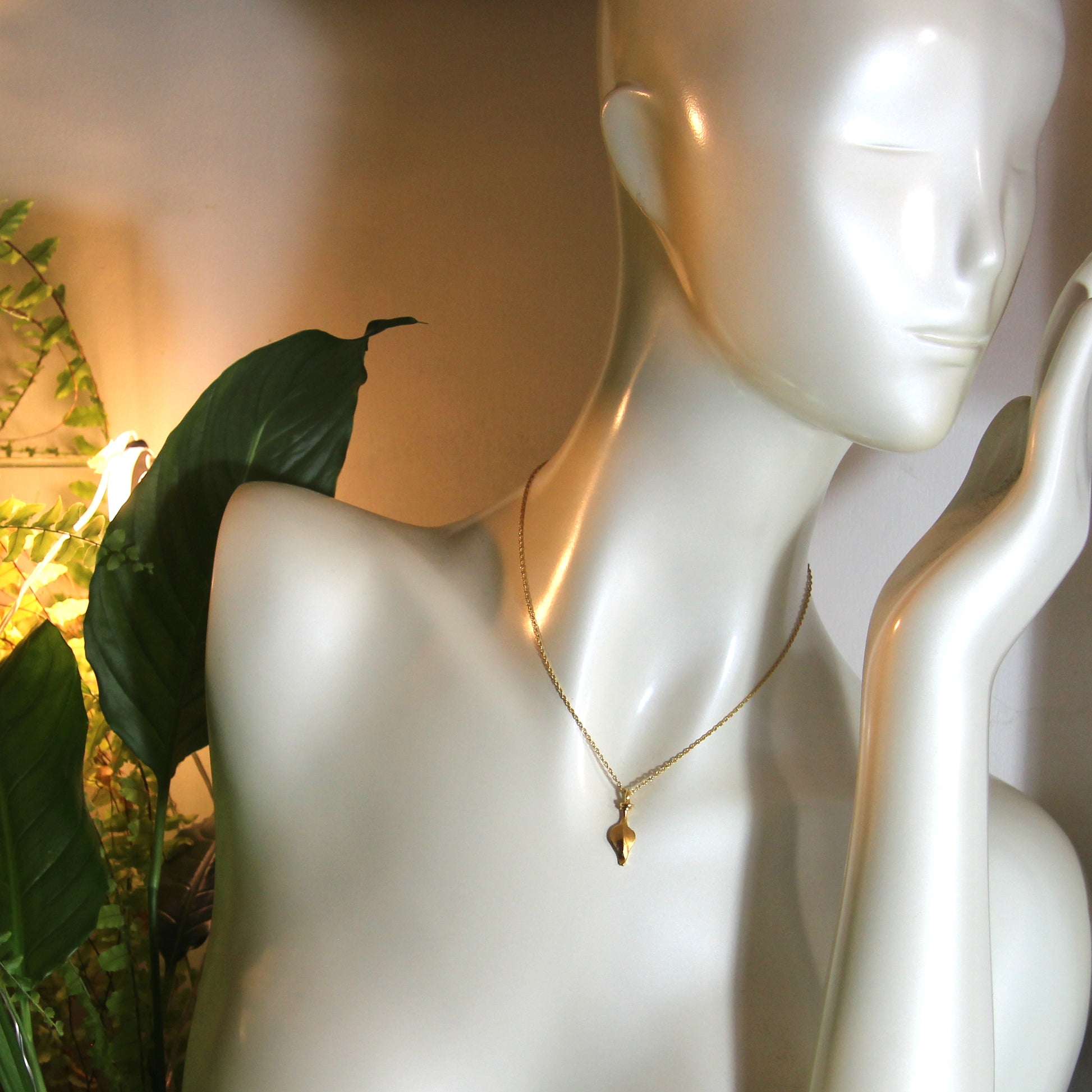 Mannequin wearing a gold leaf necklace with a green leaf in the background
