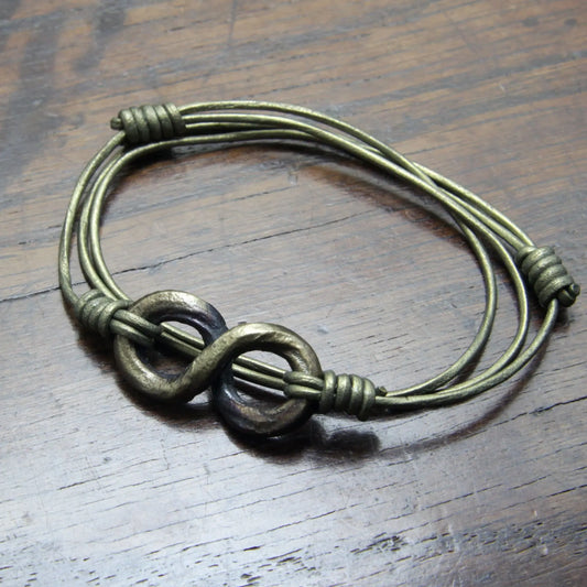 An antique bronze colored iron bracelet with  infinity loop, displayed on a dark wooden surface.