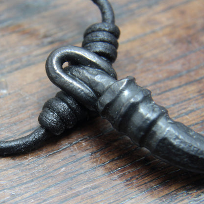 A forged iron cornicello, Italian horn, pendant with a black finish, on a black leather cord, designed and made by M Barran at Taitaya Forge.  Close up photo of the bail