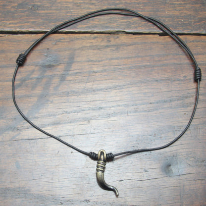 A forged iron cornicello, Italian horn, pendant with a antique bronze finish, on a black leather cord, designed and made by M Barran at Taitaya Forge.  Flat shot of whole pendant with necklace