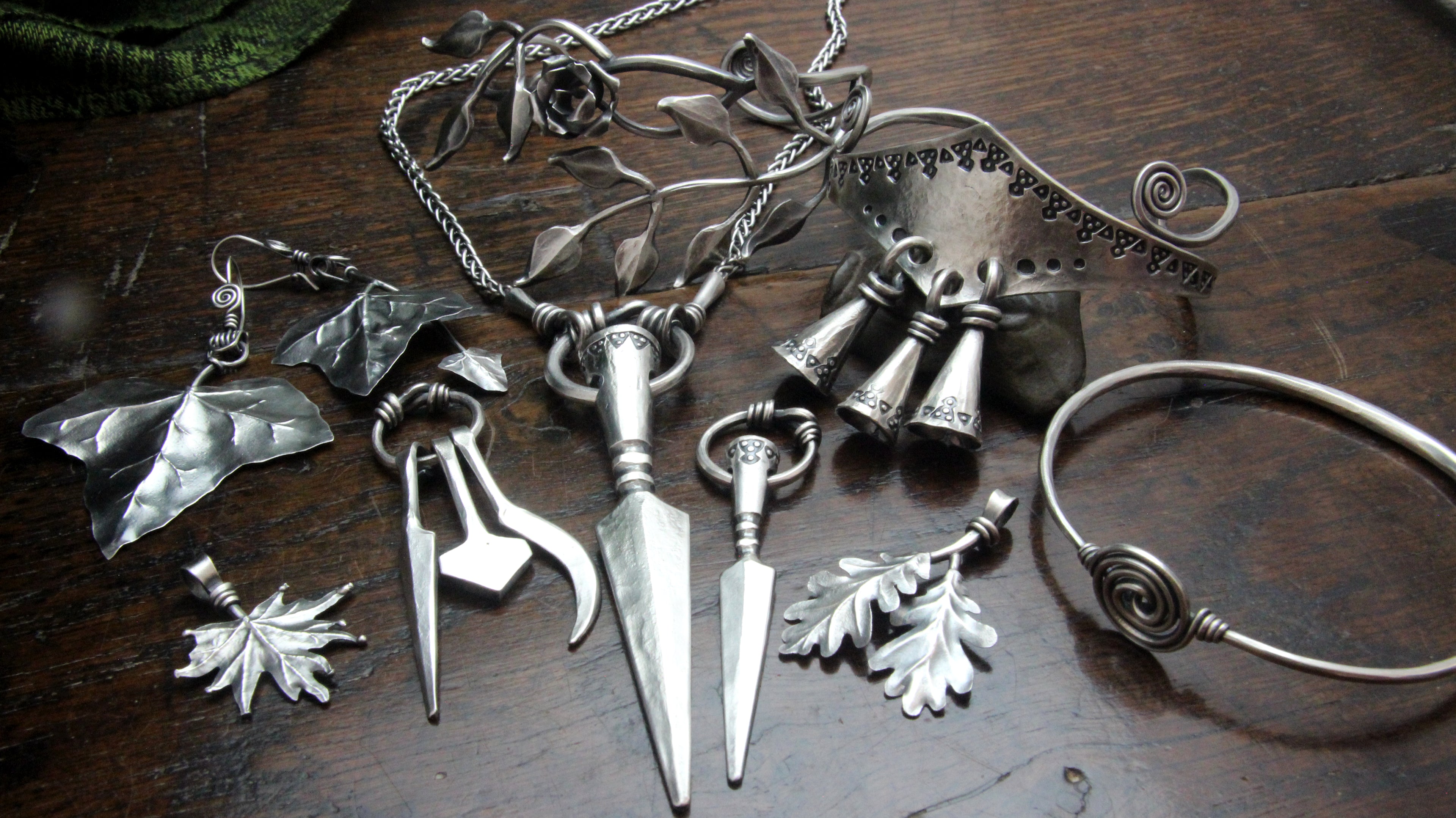 Collection of unique forged silver jewelry including pendants, a necklaces, and bracelets on a wooden surface.