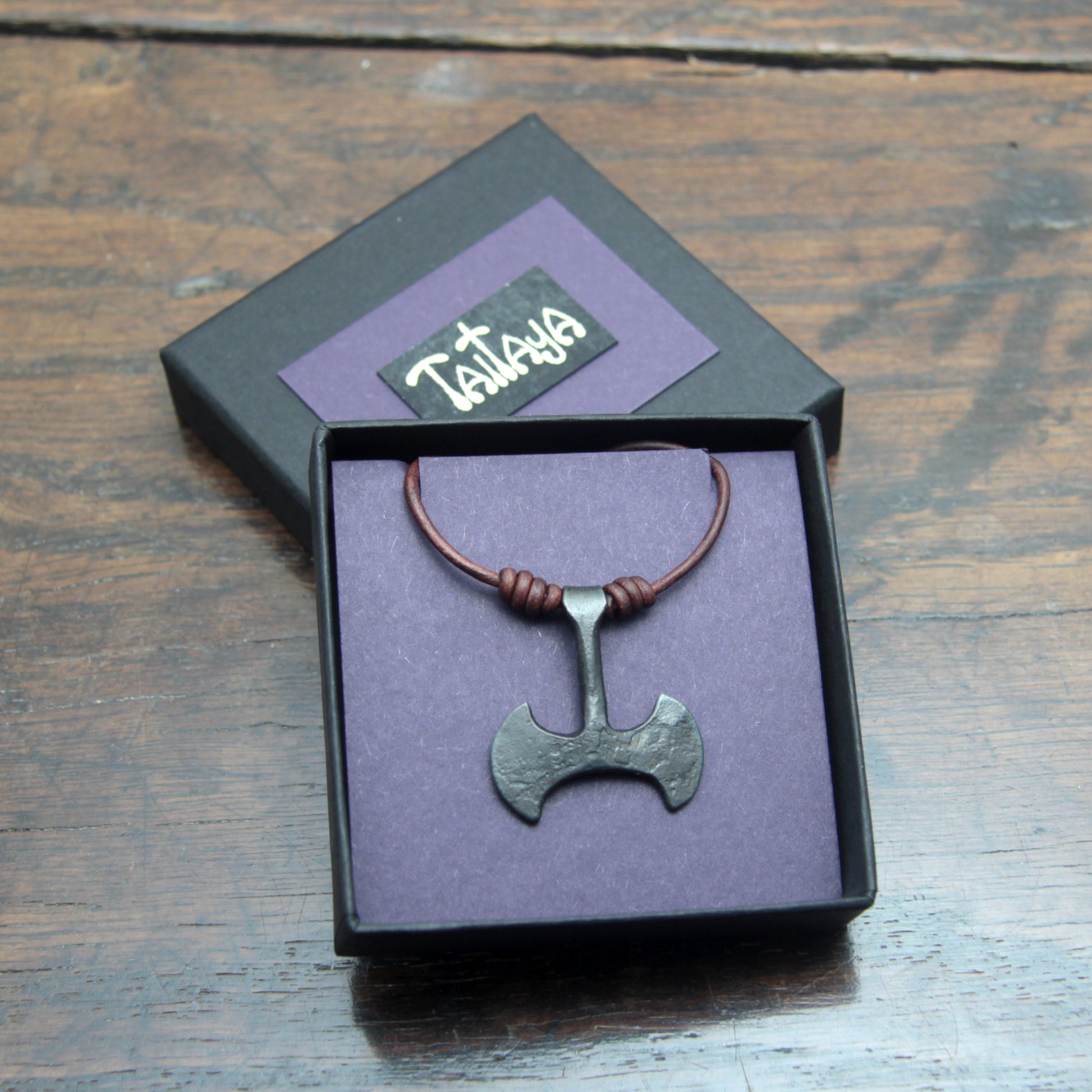 Picture of the Taitaya Forge iron Labrys pendant in a black card gift box with a purple insert and gold branding. 
