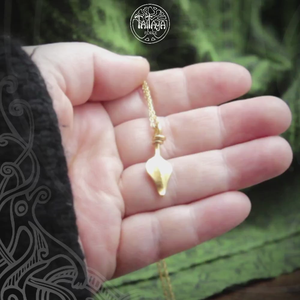 Hand holding a small gold coloured forged silver pendant on a rope chain. Green background with Taitaya branding and watermarks.